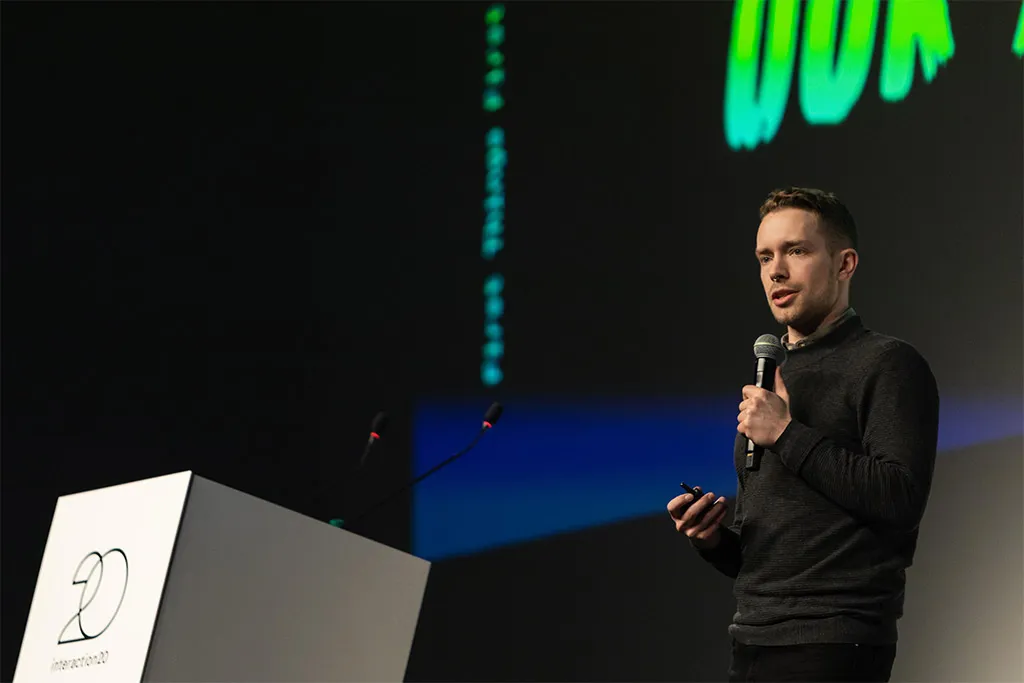 Alexis in 2020, speaking at a podium in Milan, announces the location for the Interaction 21 conference.