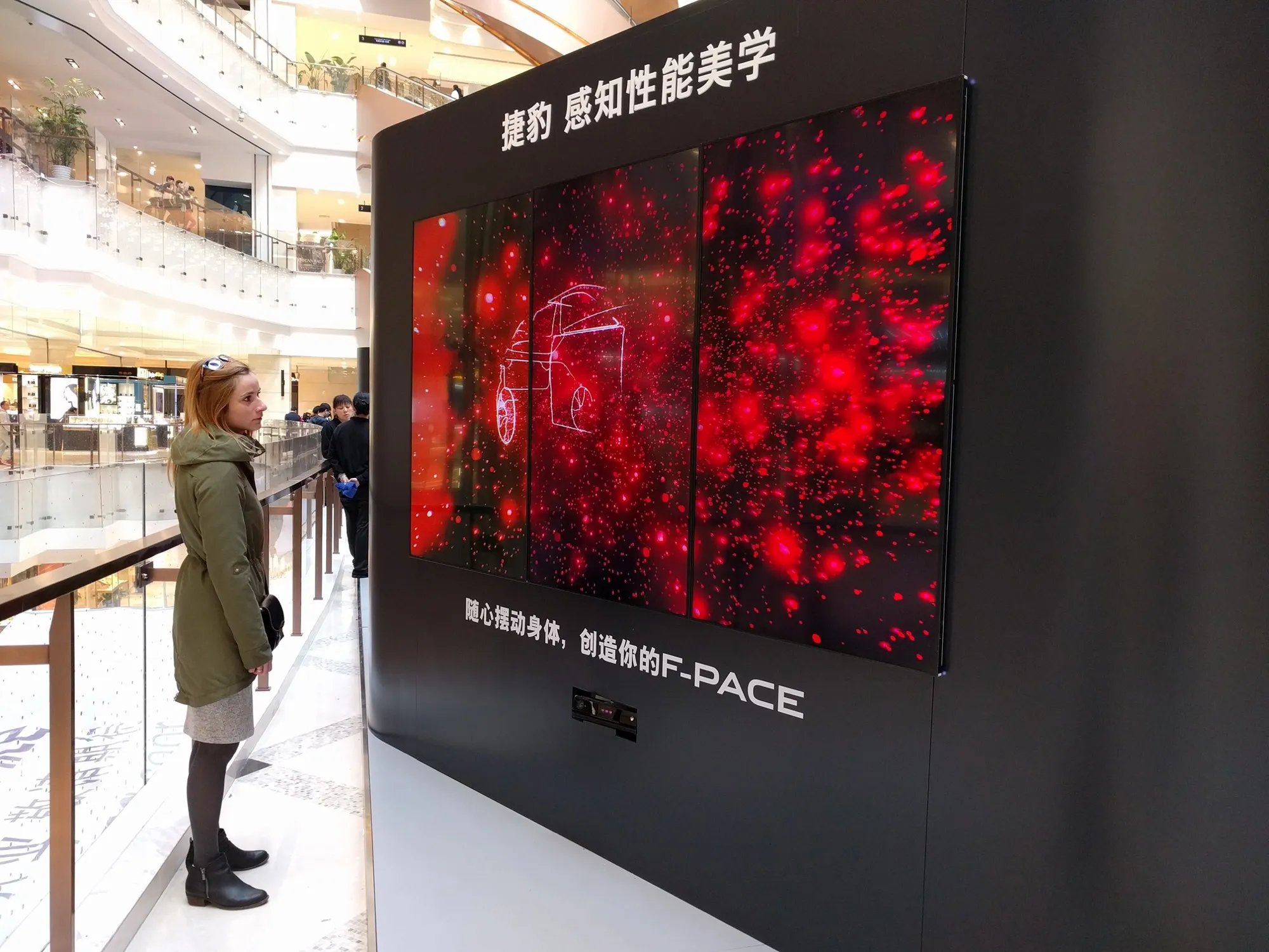 A woman standing in from of 3 TV showing red particles in the shape of a Jaguar